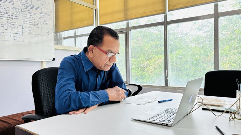 Focused man in blue shirt works intently on a laptop in a bright office setting.